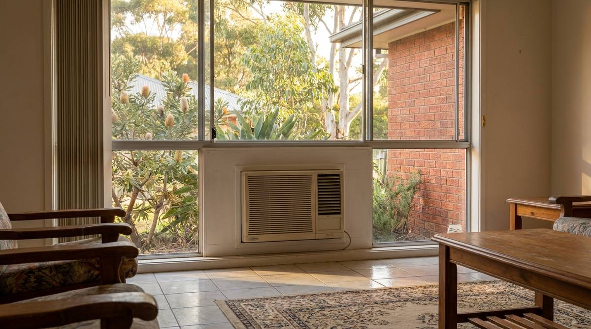 A box-style window air conditioner fitted into the lower section of a window in an Australian living room