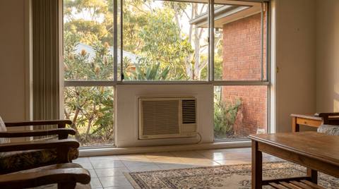 A box-style window air conditioner fitted into the lower section of a window in an Australian living room